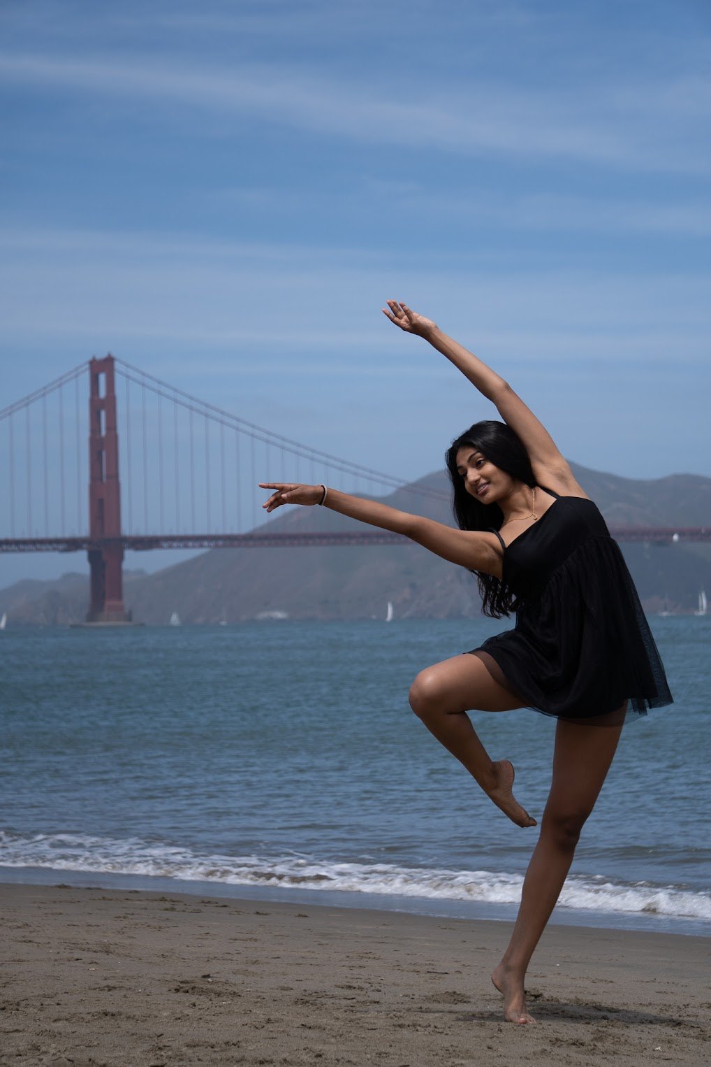 Mahika Valluri dancing on a beach with the Golden Gate Bridge behind her