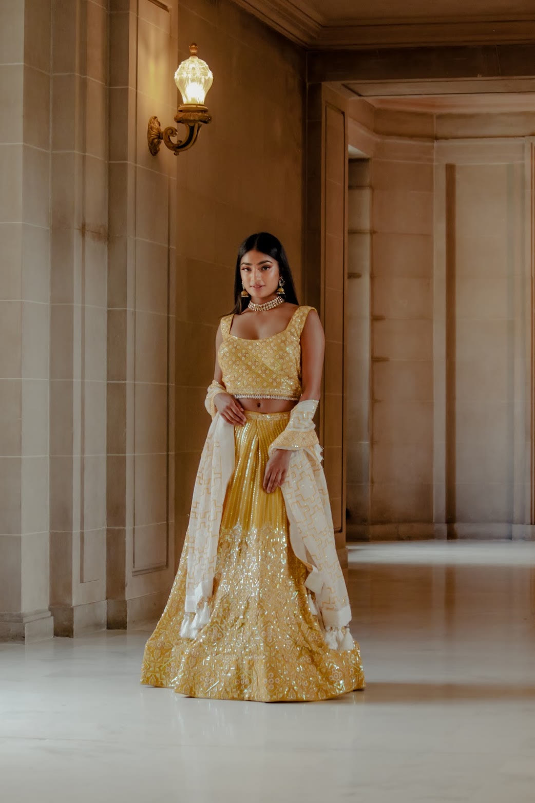 Mahika Valluri in a gold sequin lehenga in a stone hallway