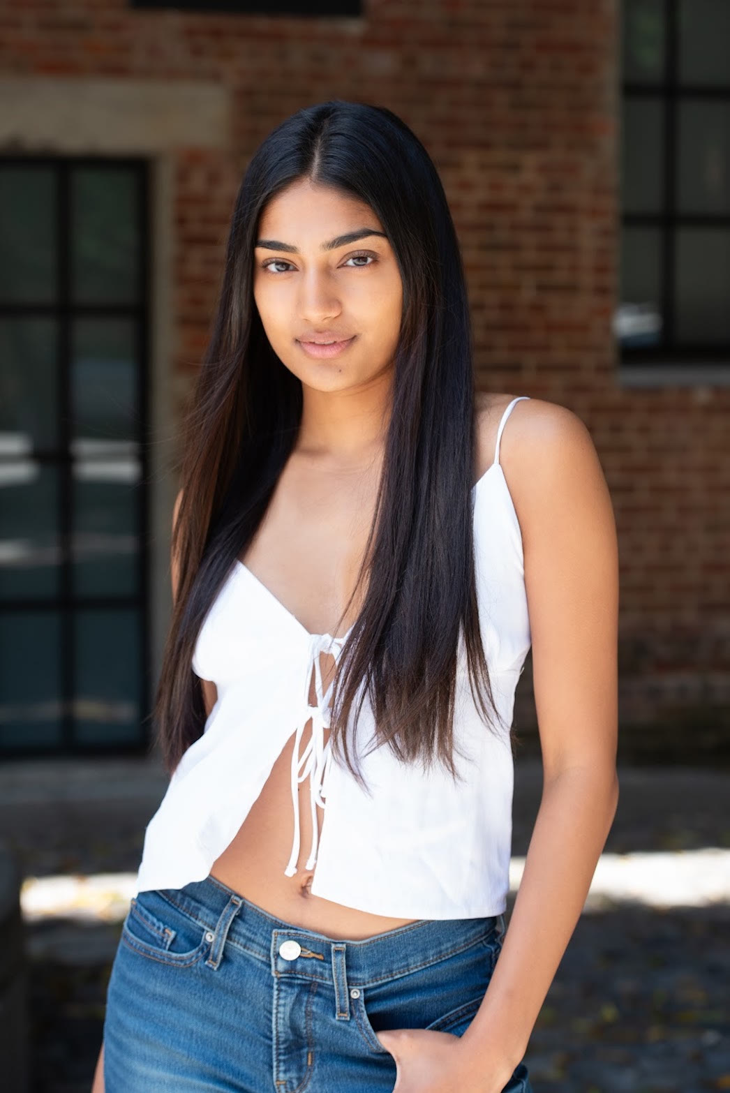 Mahika Valluri, outdoor portrait in a white tie-front top against a brick wall