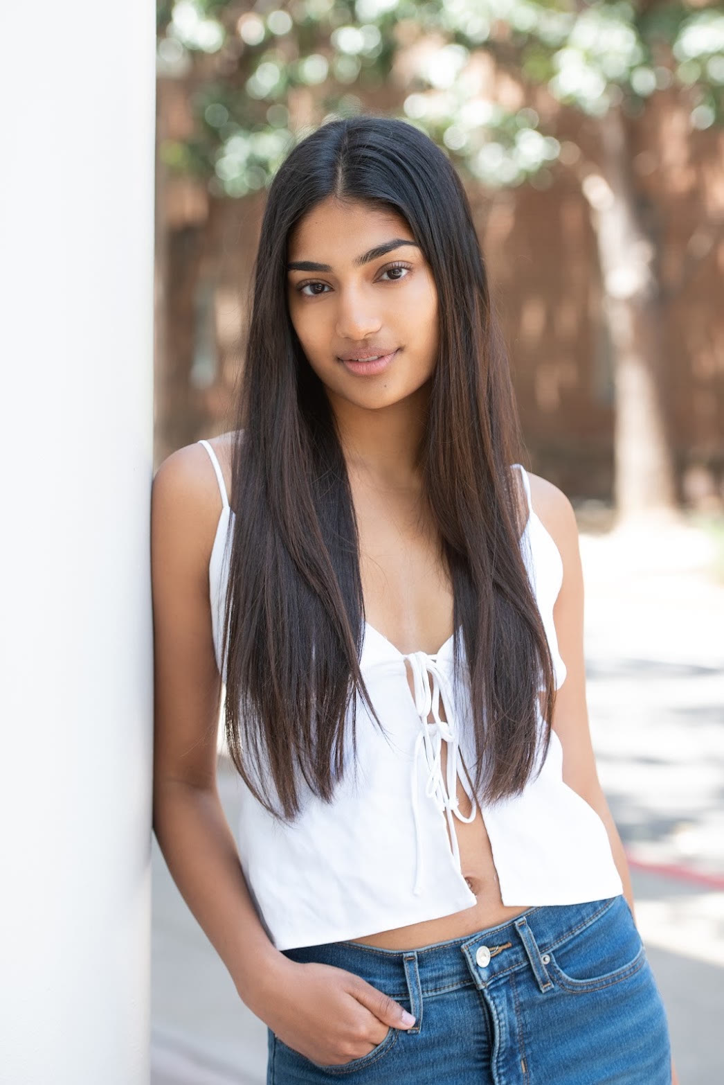 Mahika Valluri acting headshot outdoors, leaning against a white column