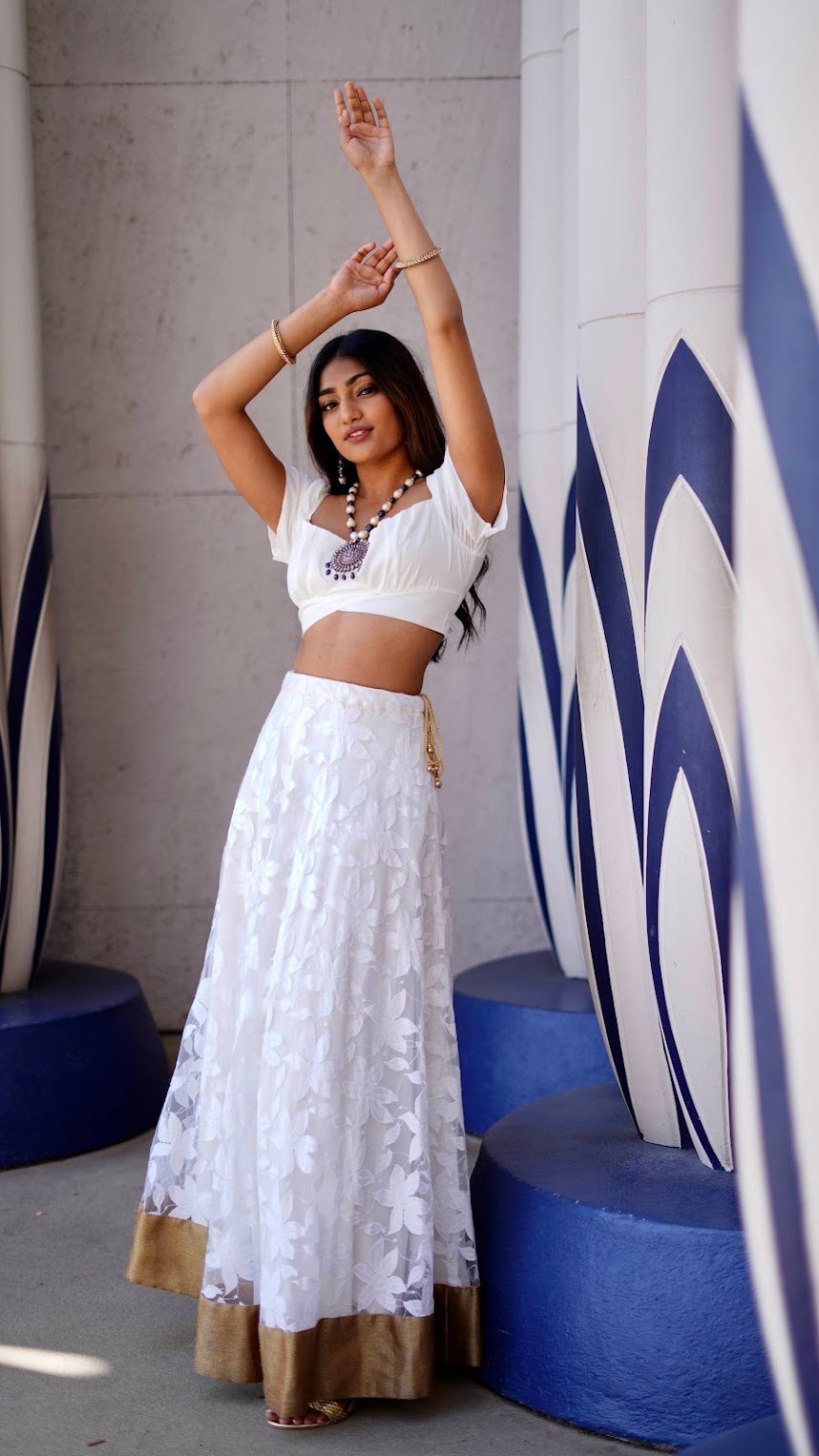 Mahika Valluri in a white floral lehenga with a gold border, one arm lifted